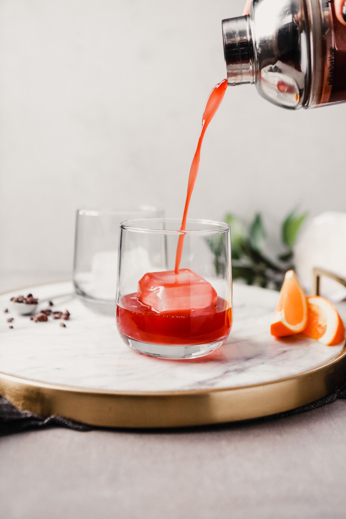Photograph of a negroni cocktail being pouring into a rocks glass set on a white marble tray.