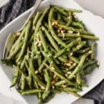 Roasted green beans with pine nuts in a square white serving dish.