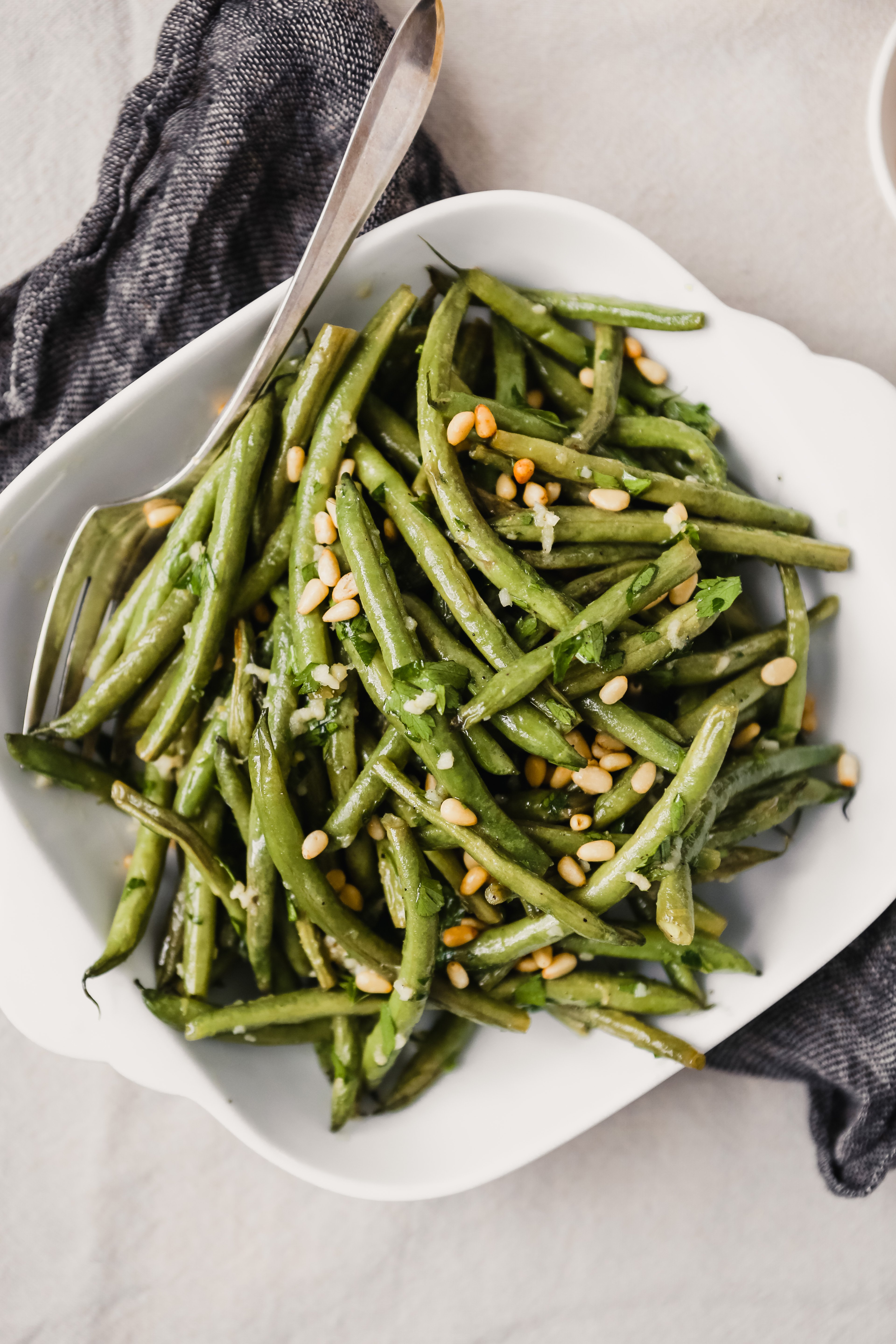 Roasted green beans with pine nuts in a square white serving dish. 