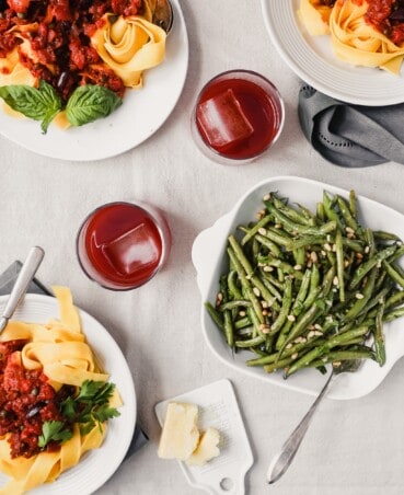 Photograph of an Italian dinner spread, green beans in a white bowl, glasses of Negroni and plates of pasta with red sauce