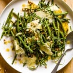 Roasted green beans, vinaigrette, cheese, pine nuts and basil on a large white serving plate with a silver brushed spoon.