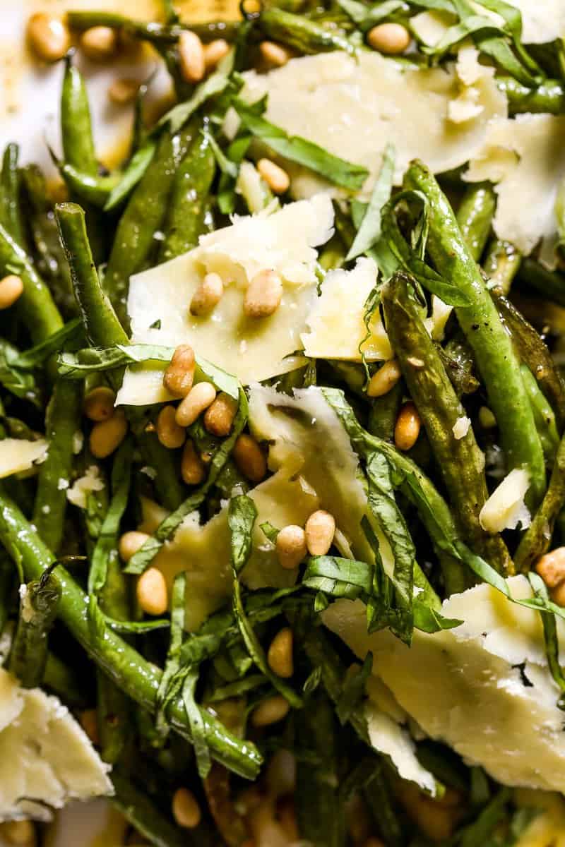 Green beans, vinaigrette, cheese, pine nuts and basil on a large white serving plate with a silver brushed spoon.