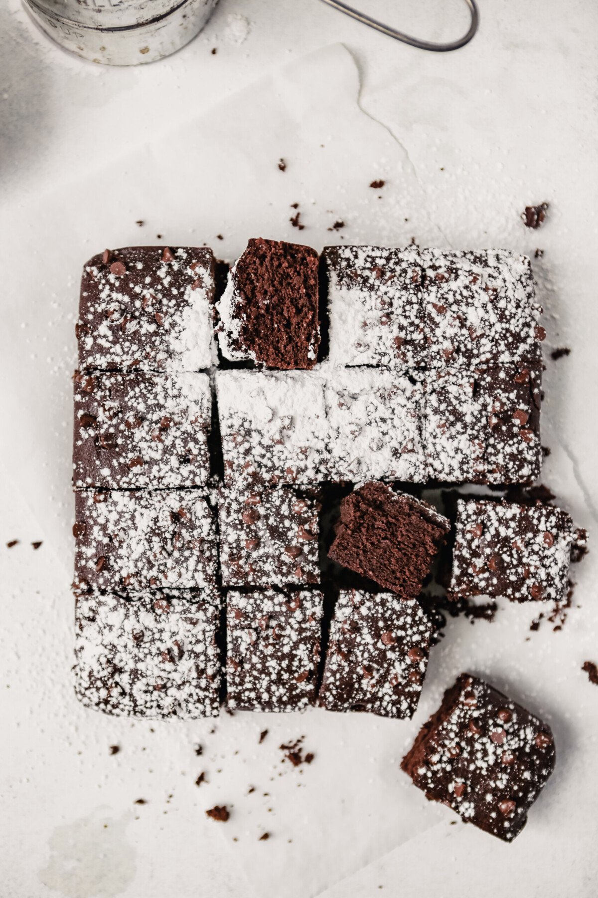 Photograph of a batch of brownies on a white surface cut into squares and dusted with powdered sugar