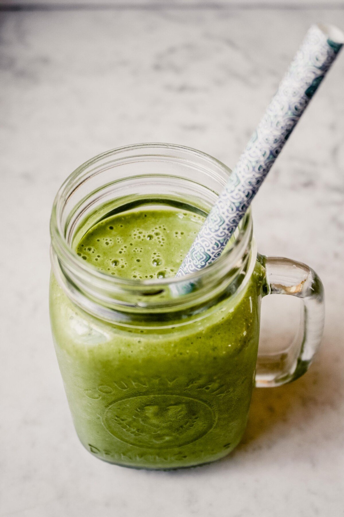 Photograph of a green kale smoothie in a glass Ball jar with a blue straw