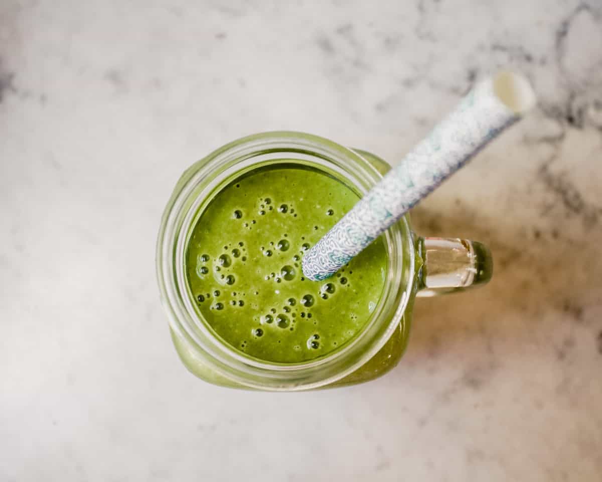 Photograph of a green kale smoothie in a glass Ball jar with a blue straw