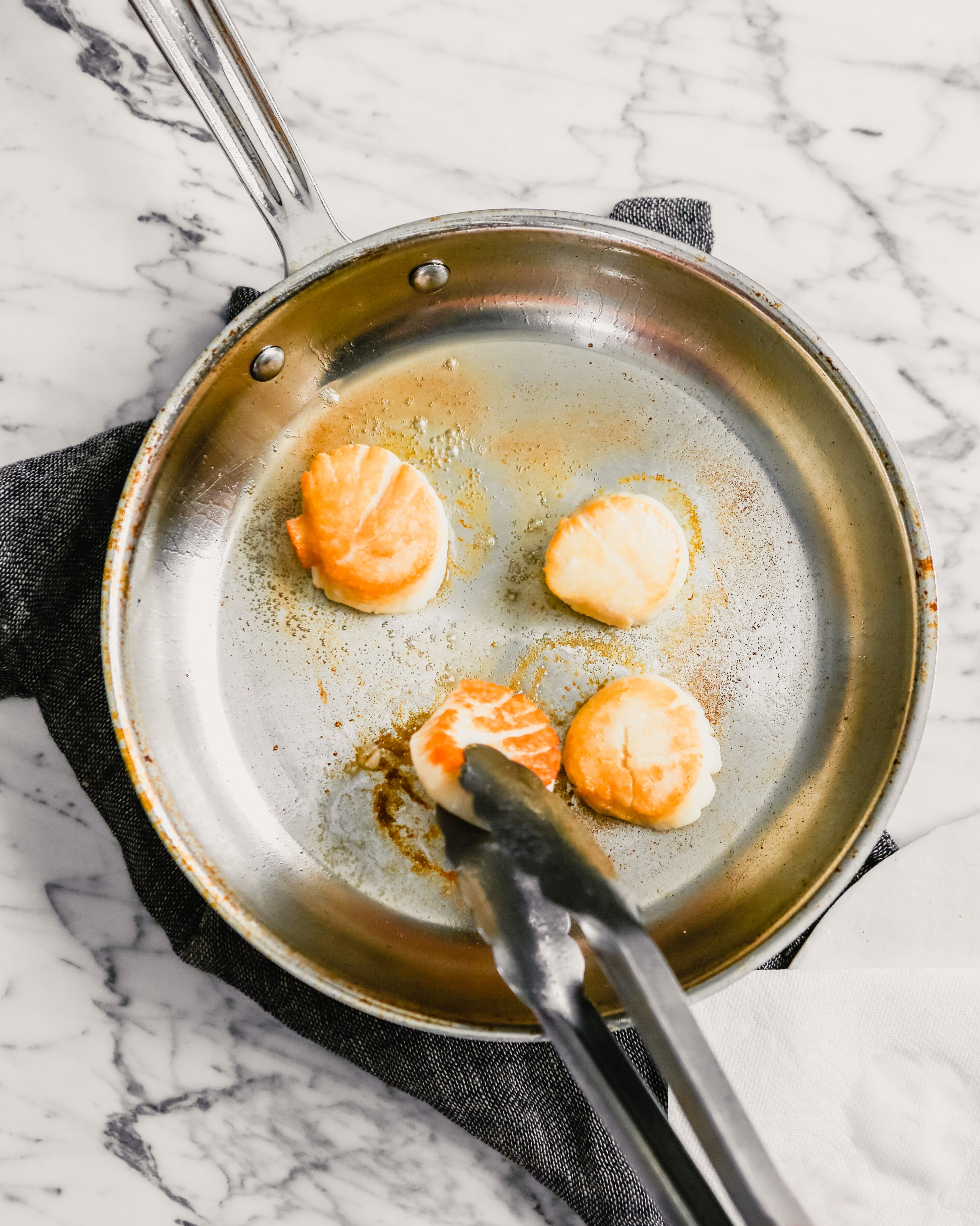 Photograph of golden brown scallops searing in a skillet.