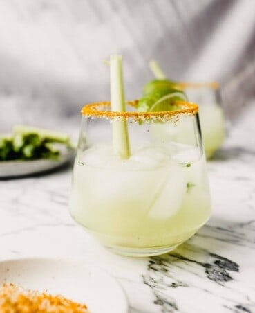 Photograph of a margarita set on a white marble table garnished with a lime wedge and lemongrass.