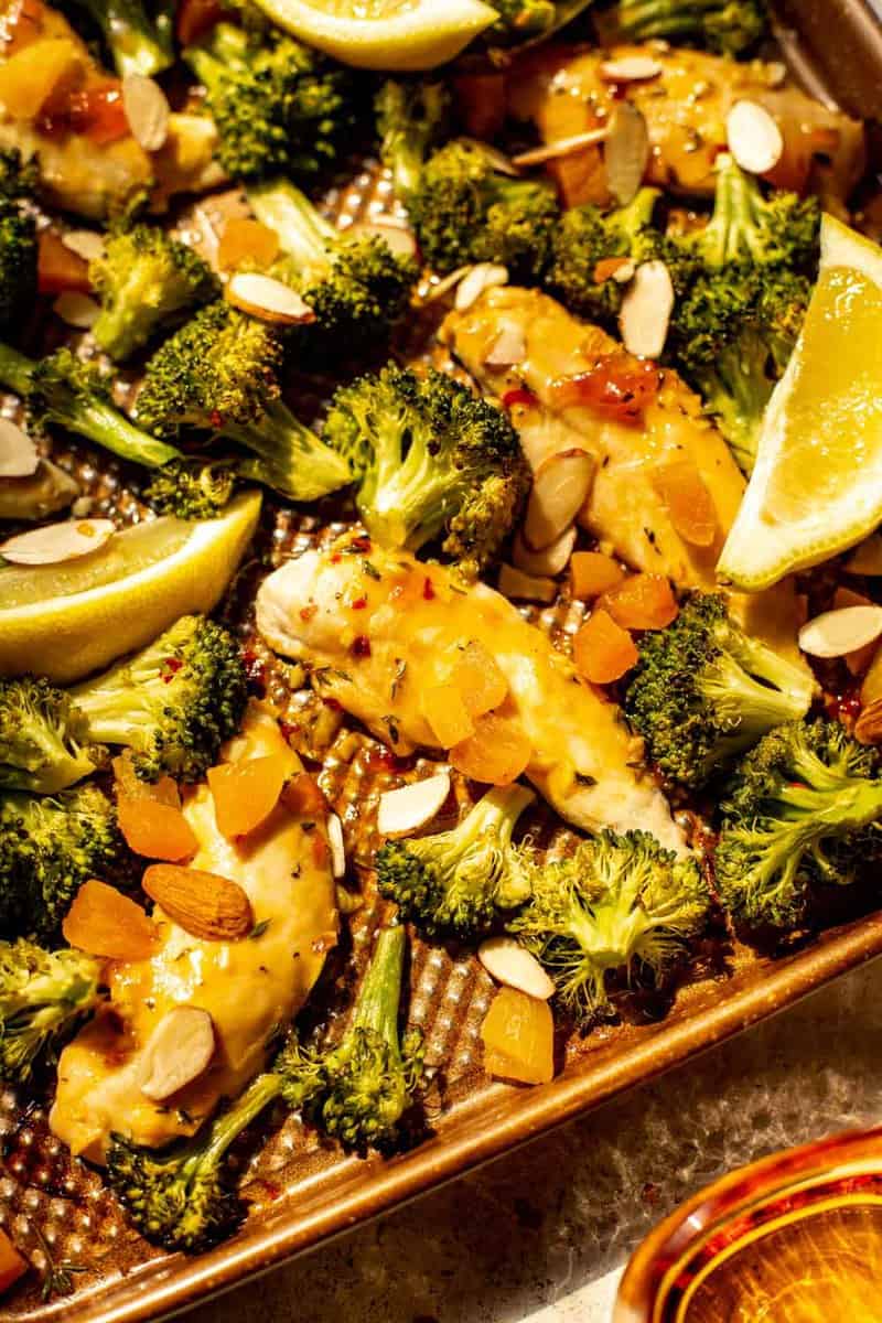 chicken tenders coated in an apricot glaze on a baking sheet with broccoli florets and diced apricots 