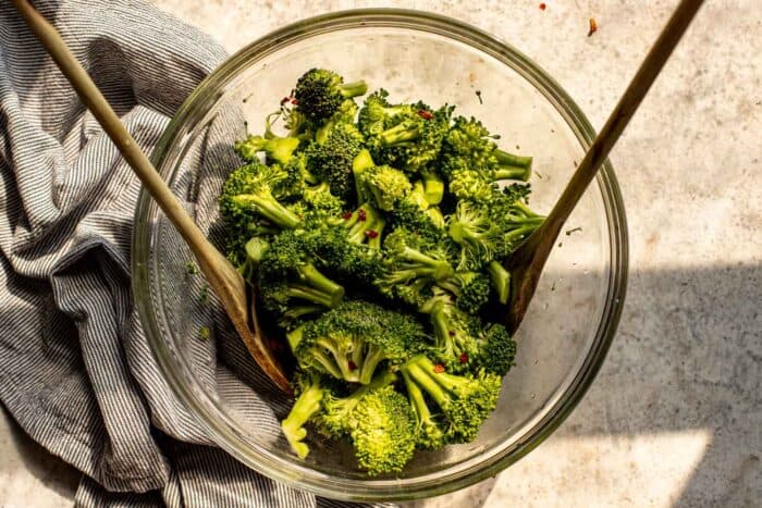 broccoli florets in a large glass bowl tossed with olive oil, salt and pepper