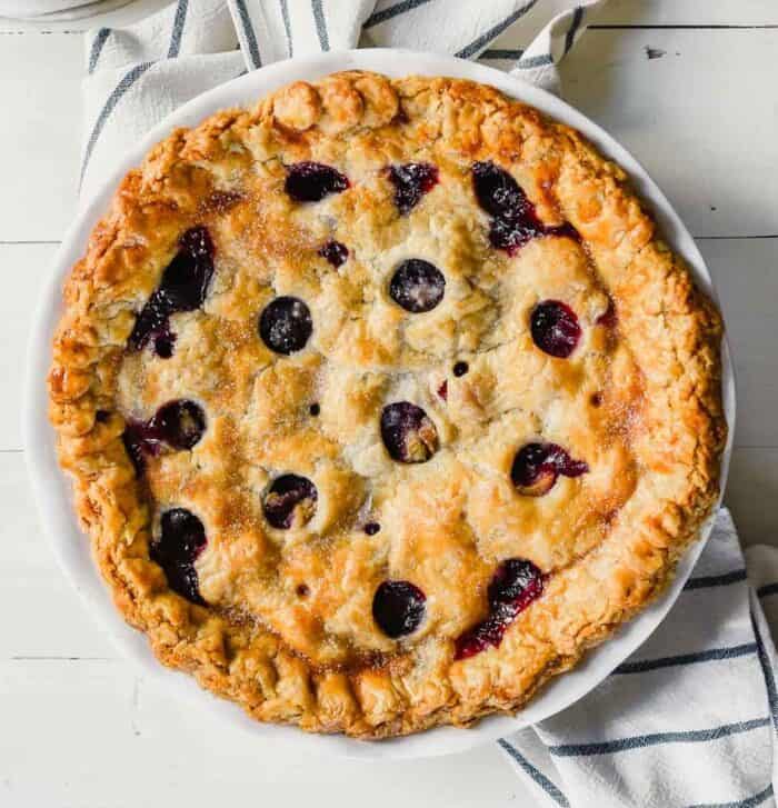 blueberry rhubarb pie set on a white table with a stripped napkin