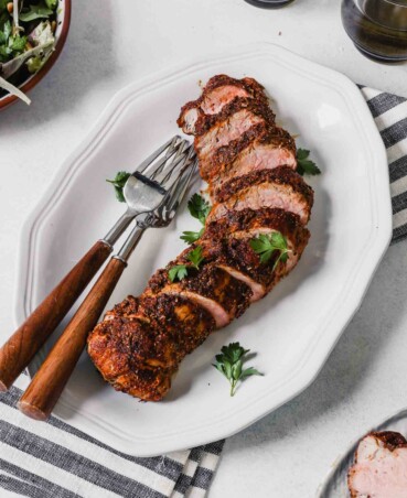 Photograph of sliced roasted pork tenderloin on a white plate