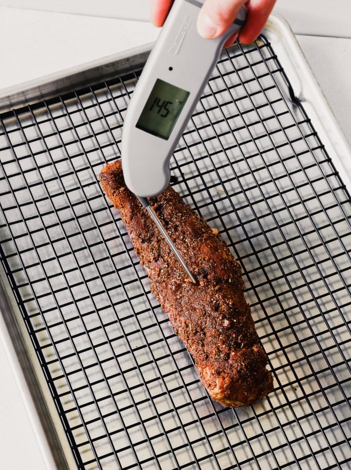Photograph of a pork tenderloin's internal temperature being checked with an instant-read thermometer.
