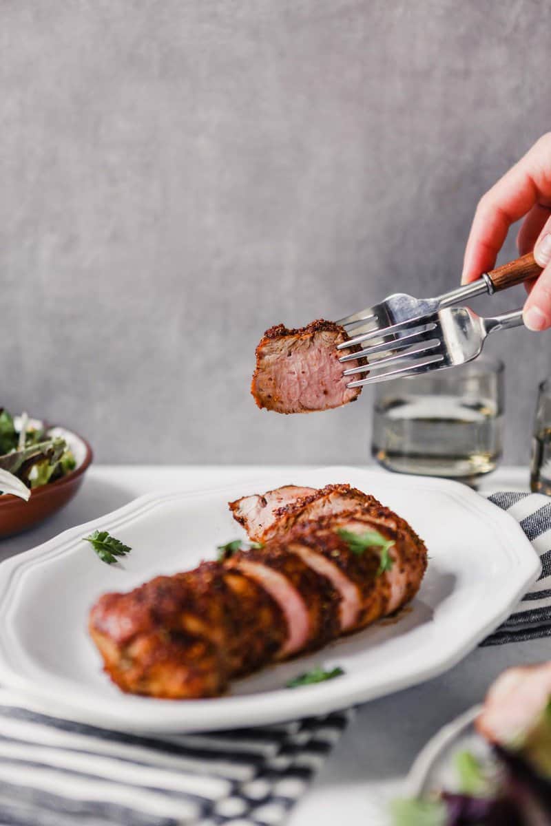 Photograph of a slice of roasted pork tenderloin being picked up with two forks