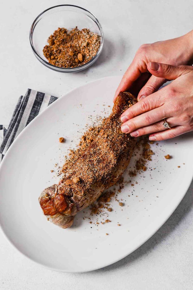 Photograph of a pork tenderloin being rubbed with a spice mixture