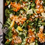 Photograph of apricot-glazed chicken on a sheet pan with broccoli, almond and lemon wedges.