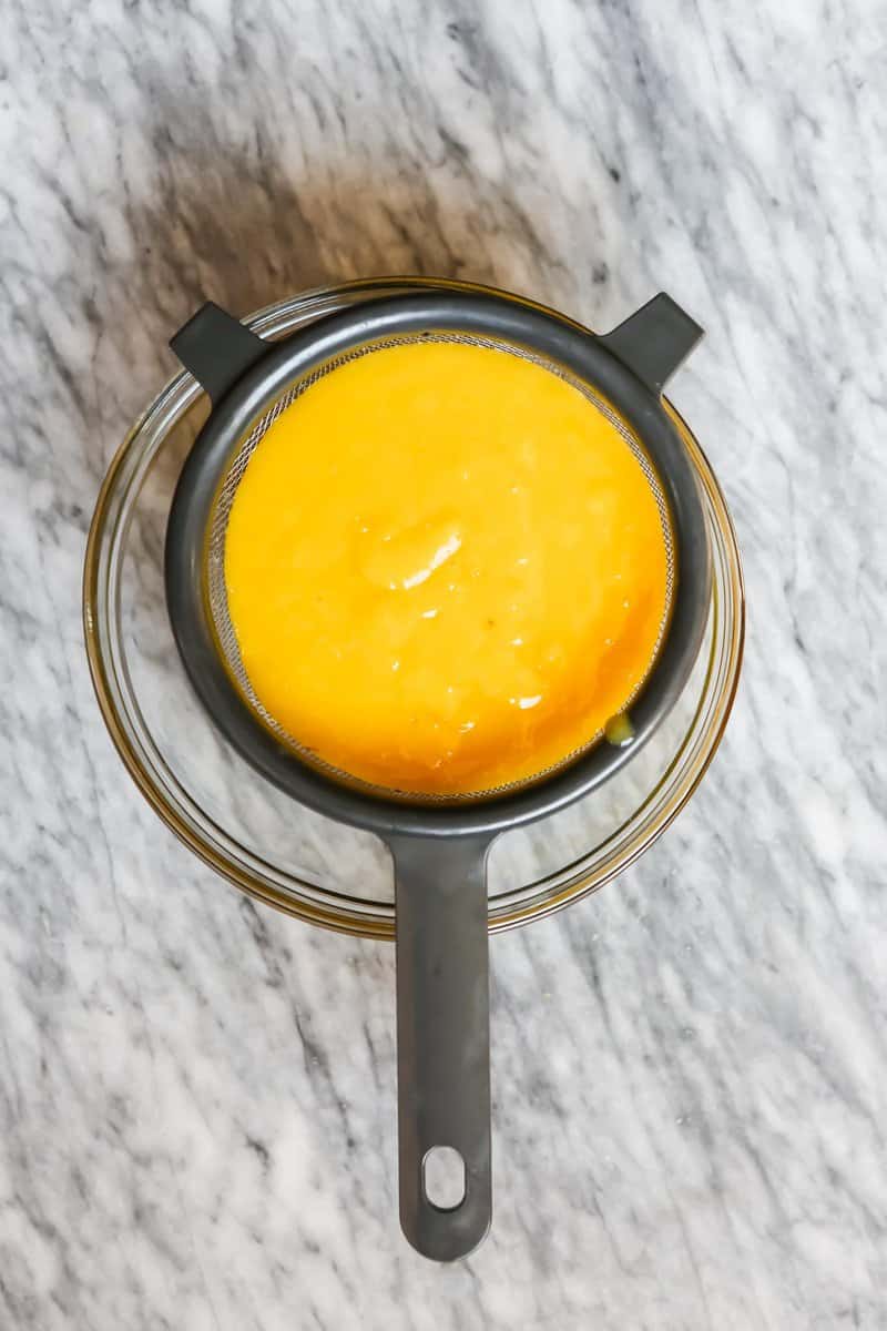 Photograph of lemon curd being strained through a fine-mesh sieve. 