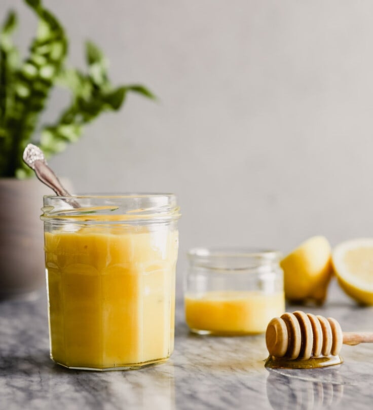 Photograph of lemon curd in a glass jar set on a marble table.