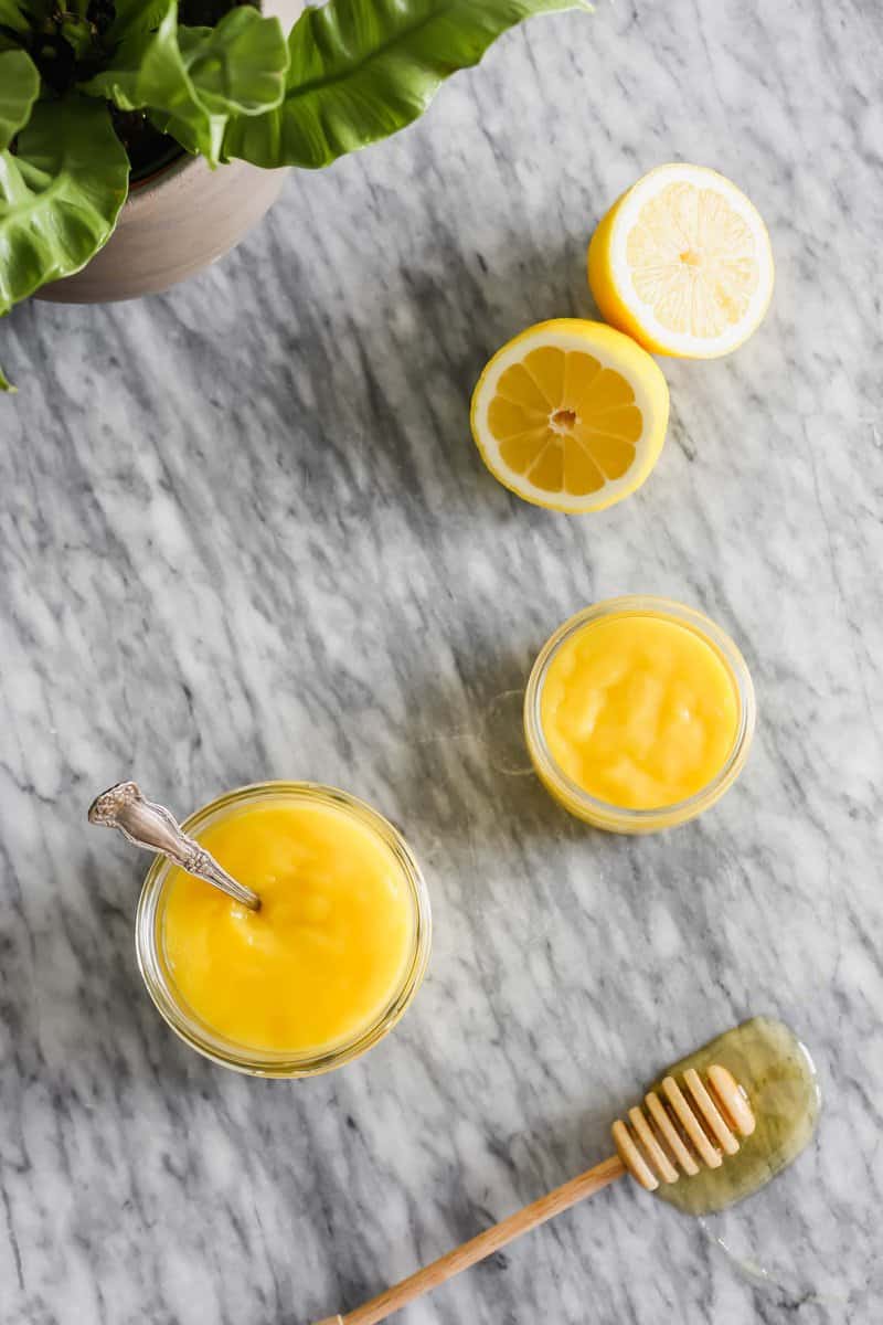 Overhead photograph of lemon curd in a glass jar set on a marble table.