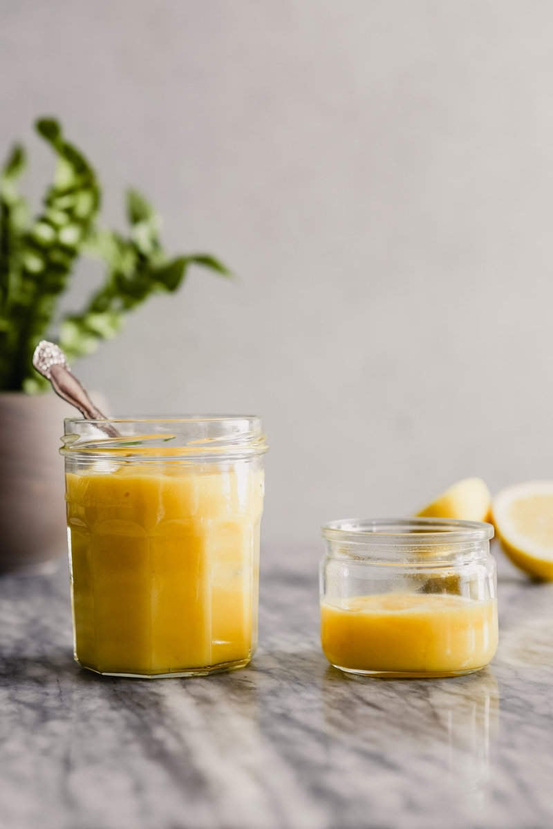 Photograph of lemon curd in a glass jar set on a marble table.