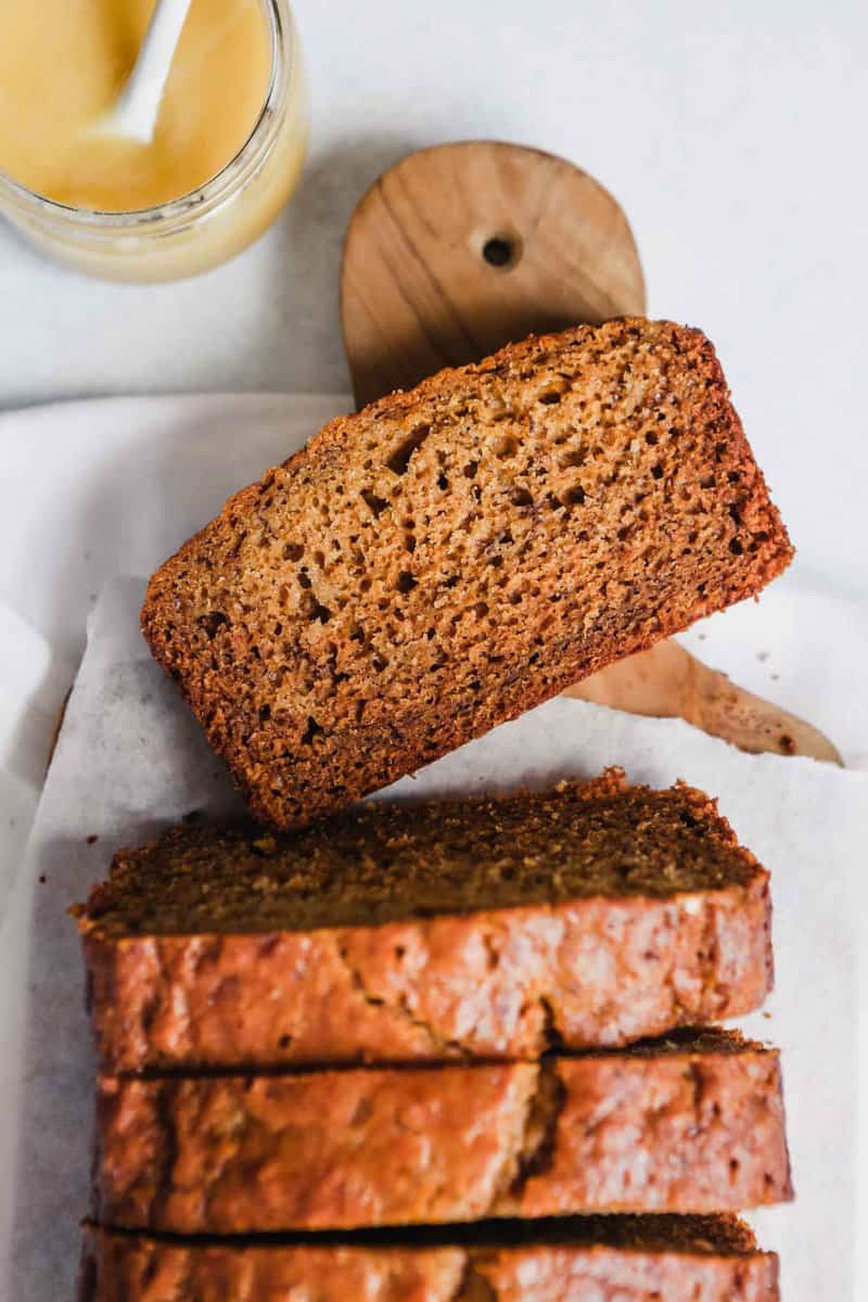 Photograph of a loaf of healthy olive oil banana bread sliced on a wooden board