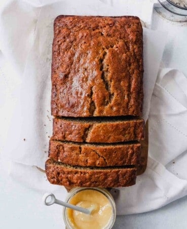 Photograph of a loaf of healthy olive oil banana bread sliced on a wooden board