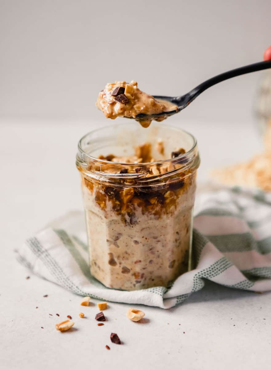 Photograph of a black spoon scooping up chocolate peanut butter overnight oats from a glass jar. 