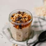 Photograph of chocolate peanut butter overnight oats in a glass jar on a table with spilled oats