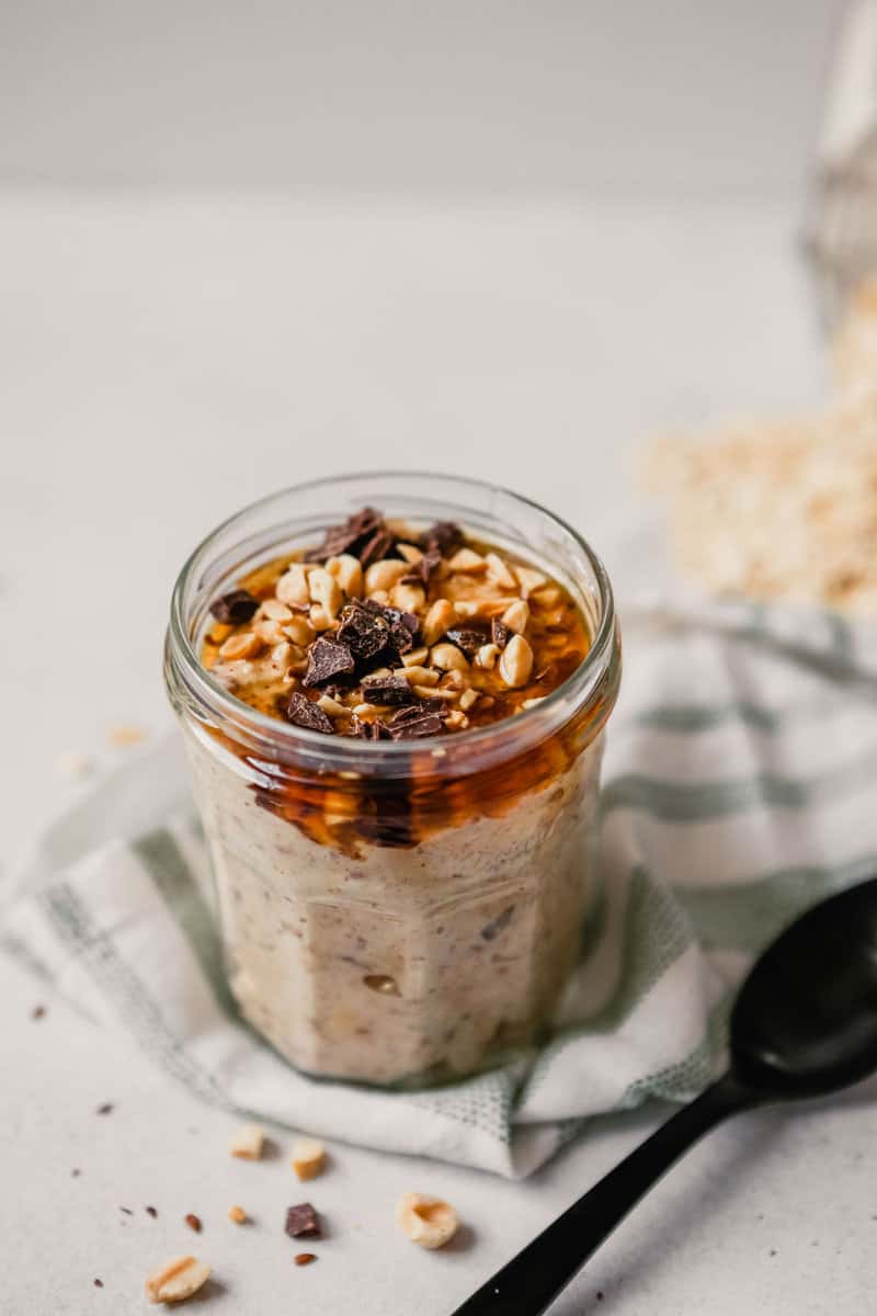 Photograph of chocolate peanut butter overnight oats in a glass jar on a table with spilled oats