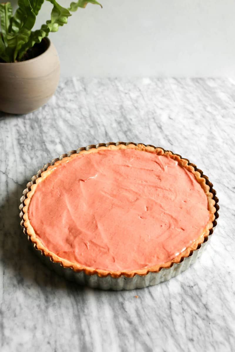 Photograph of a tart crust filled with rhubarb curd set on a marble table.