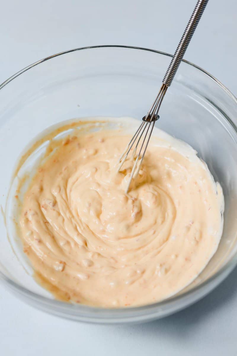 Photograph of a spicy mayonnaise in a clear mixing bowl with a whisk