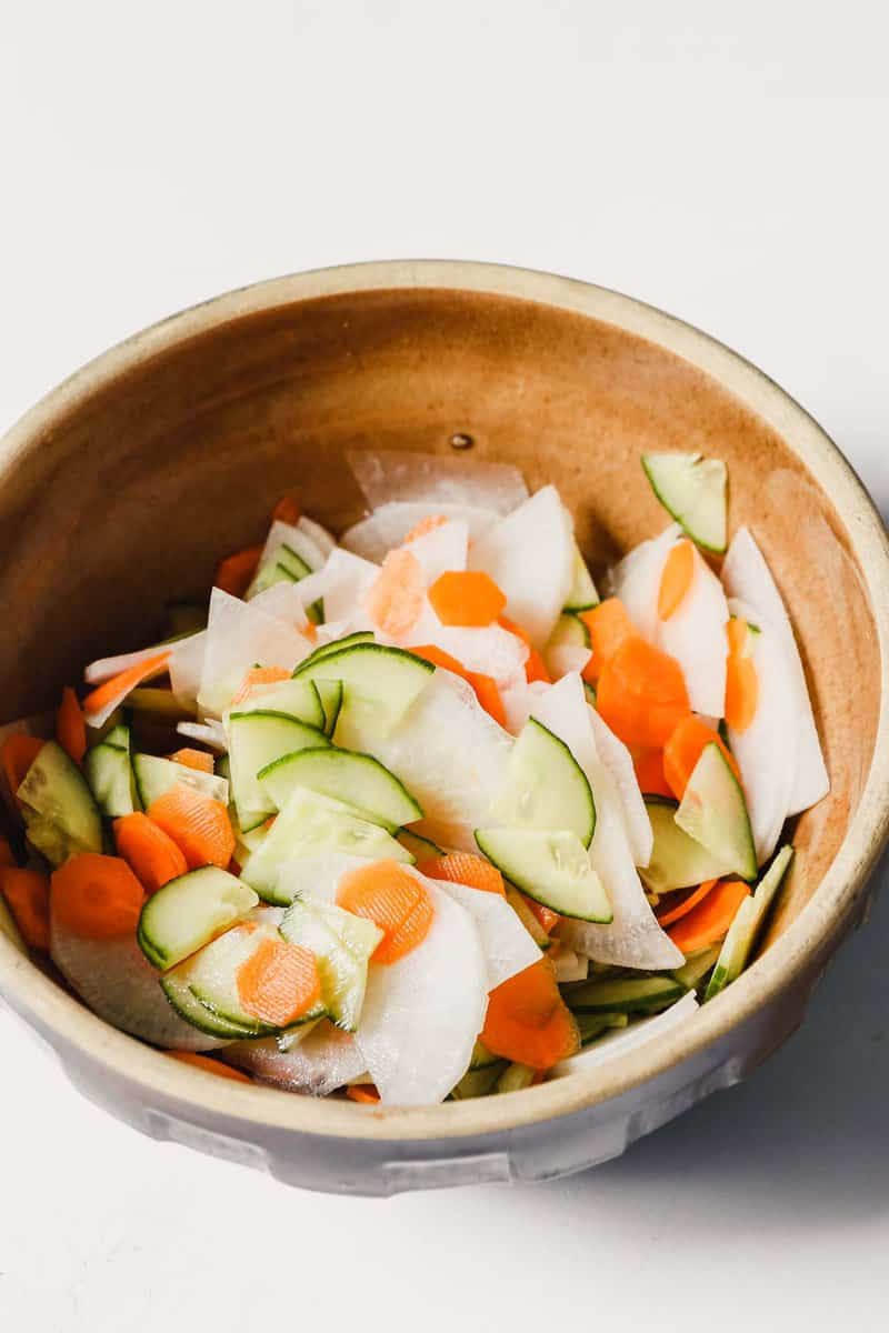 Photograph of pickled carrots, Daikon and cucumber in a brown bowl. 