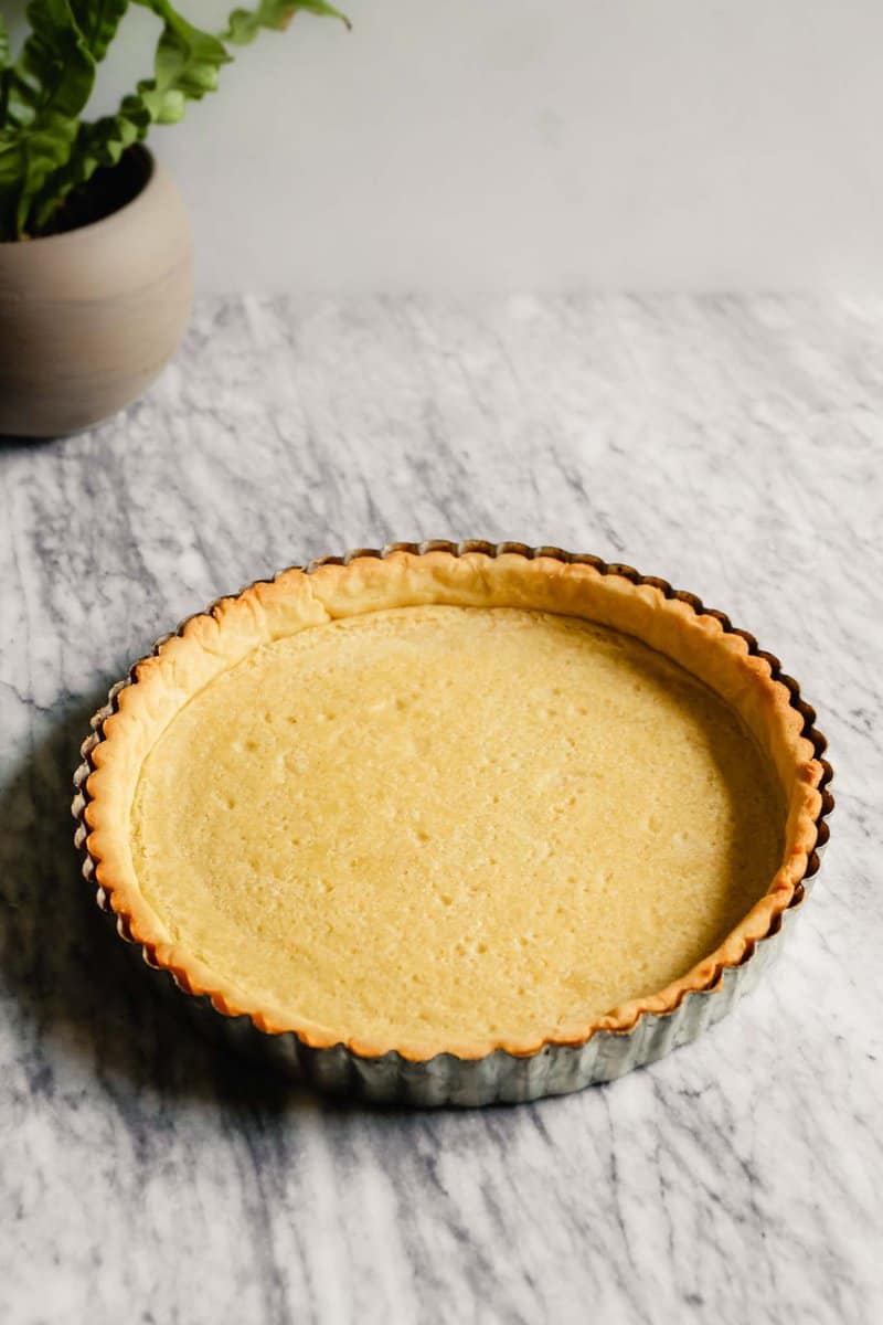 Photograph of a baked tart crust in a tart pan set on a marble table
