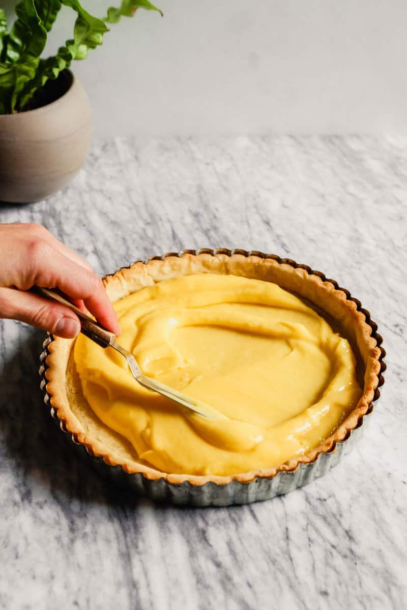 Photograph of lemon curd being spread into a tart crust.