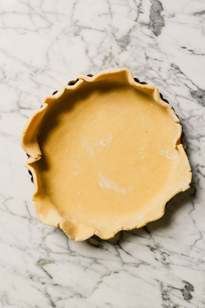 Photograph of dough placed in a tart pan set on a marble table.