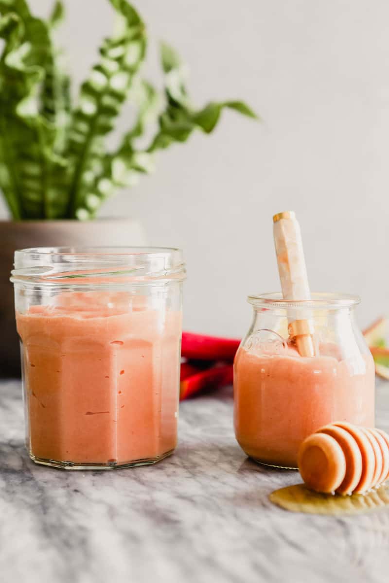 Photograph of pink rhubarb in a small jar with a hold spoon set on a marble surface.
