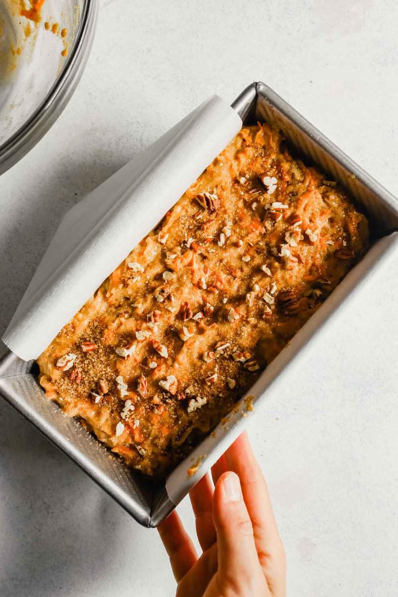 Photograph of carrot bread batter, topped with turbinado sugar and pecans, in a loaf pan