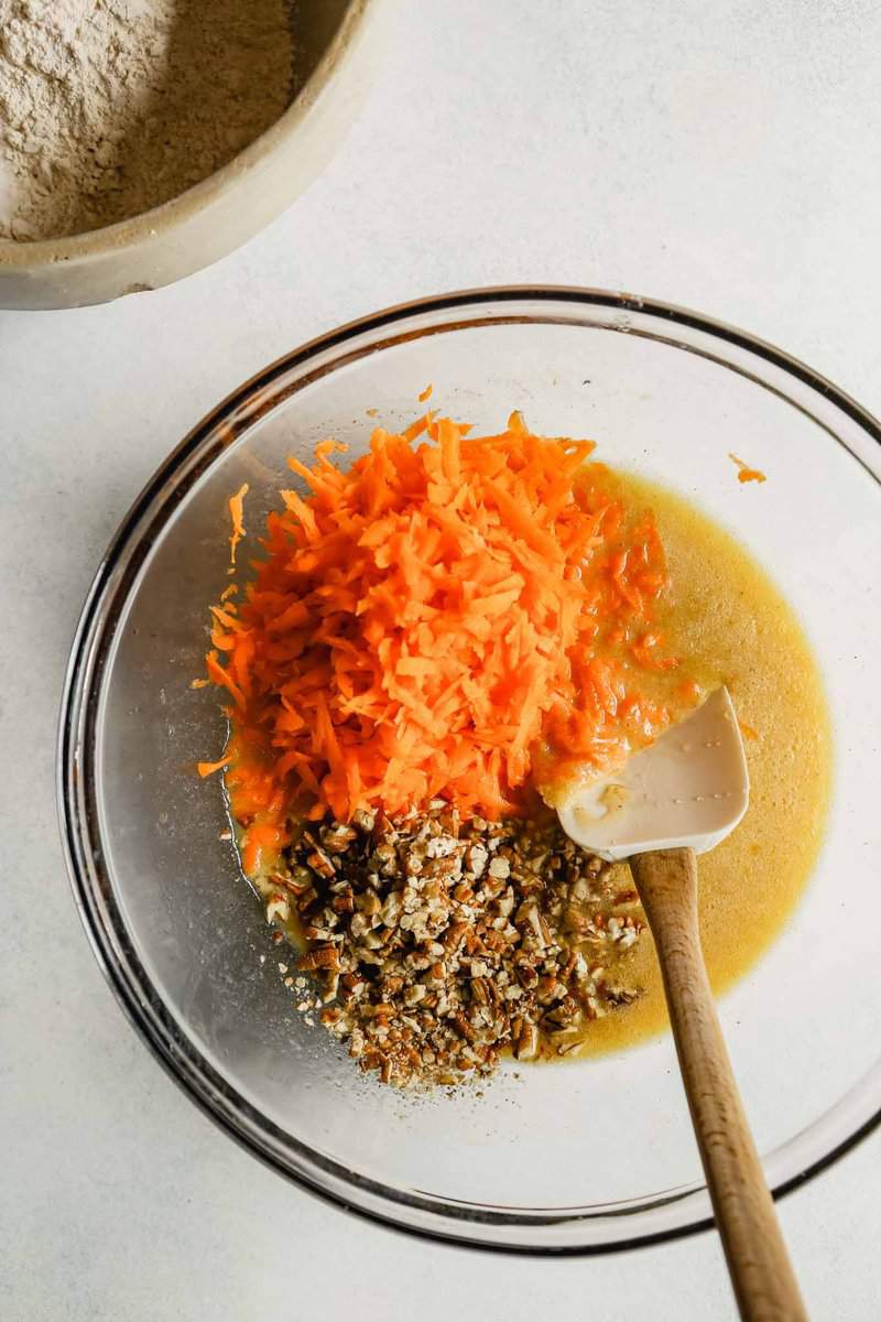 Photograph of shredded carrots and chopped pecans in a bowl with wet ingredients 