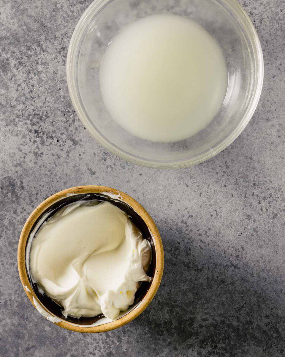 a small brown bowl filled with a creamy spread and a clear glass bowl containing milky-liquid