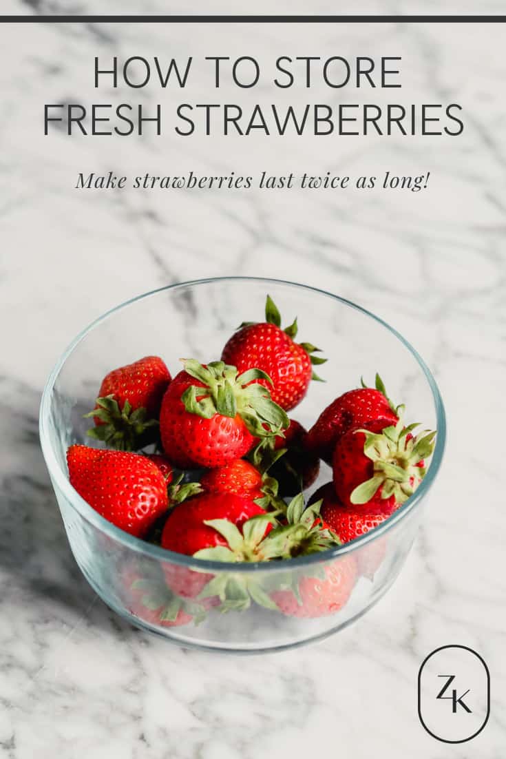 Photograph of fresh strawberries in a glass storage container set on a marble table