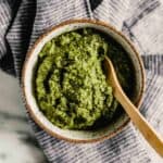 Photograph of bright green carrot top pesto in a speckled bowl
