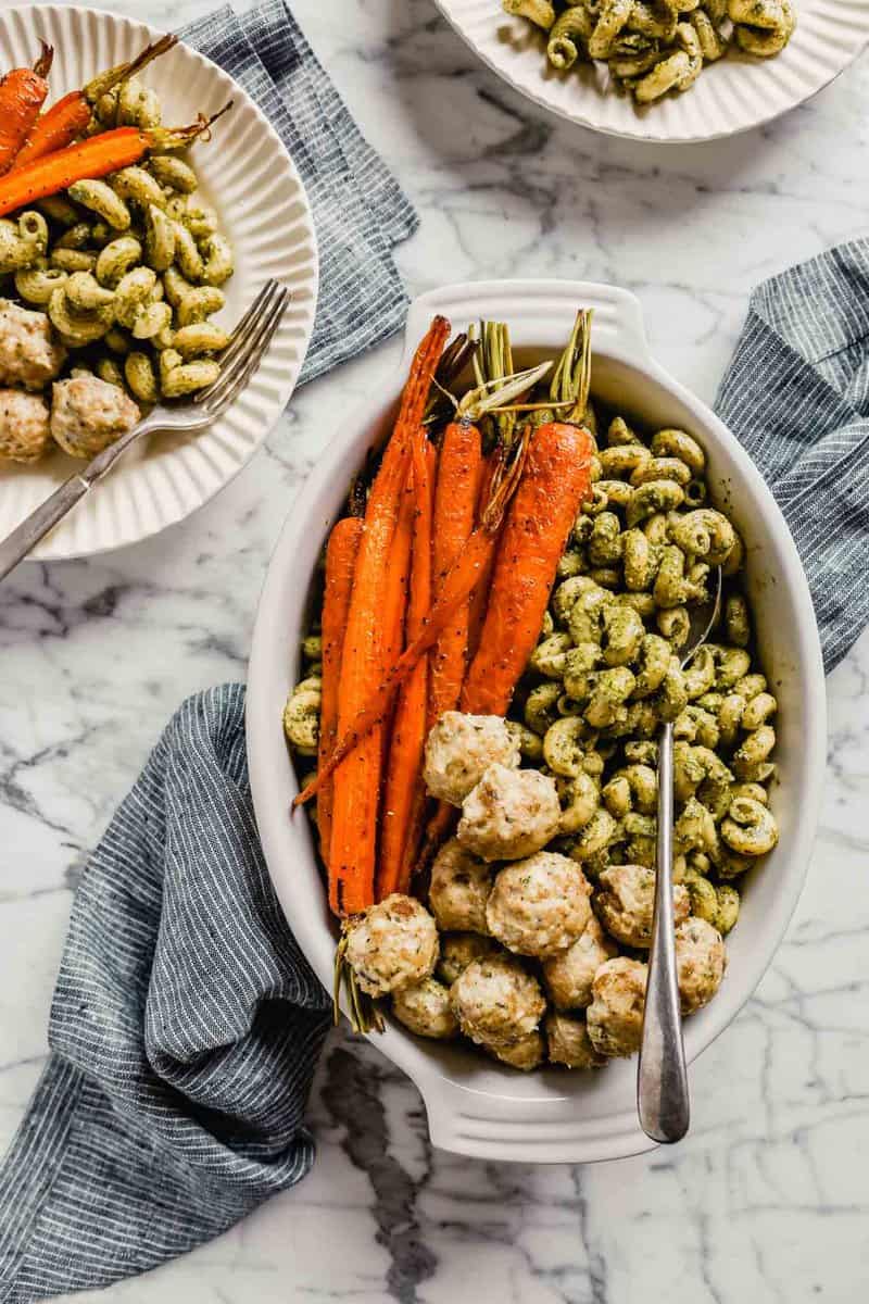 Photograph of a large serving dish filled with pesto pasta, chicken meatballs and roasted carrots