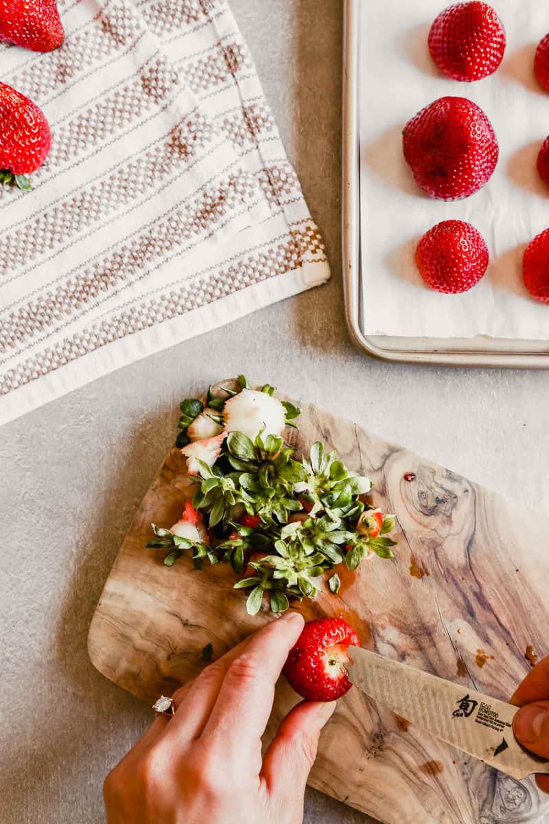 Photograph of someone hulling a fresh strawberry with a paring knife 