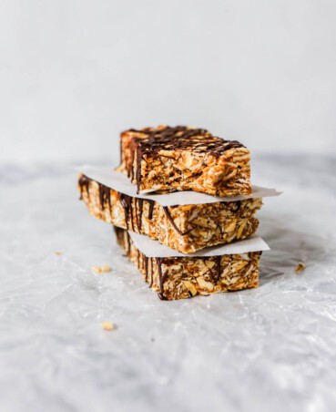 Photograph of homemade chewy granola bars stacked on top of each other on wax paper on a marble table.