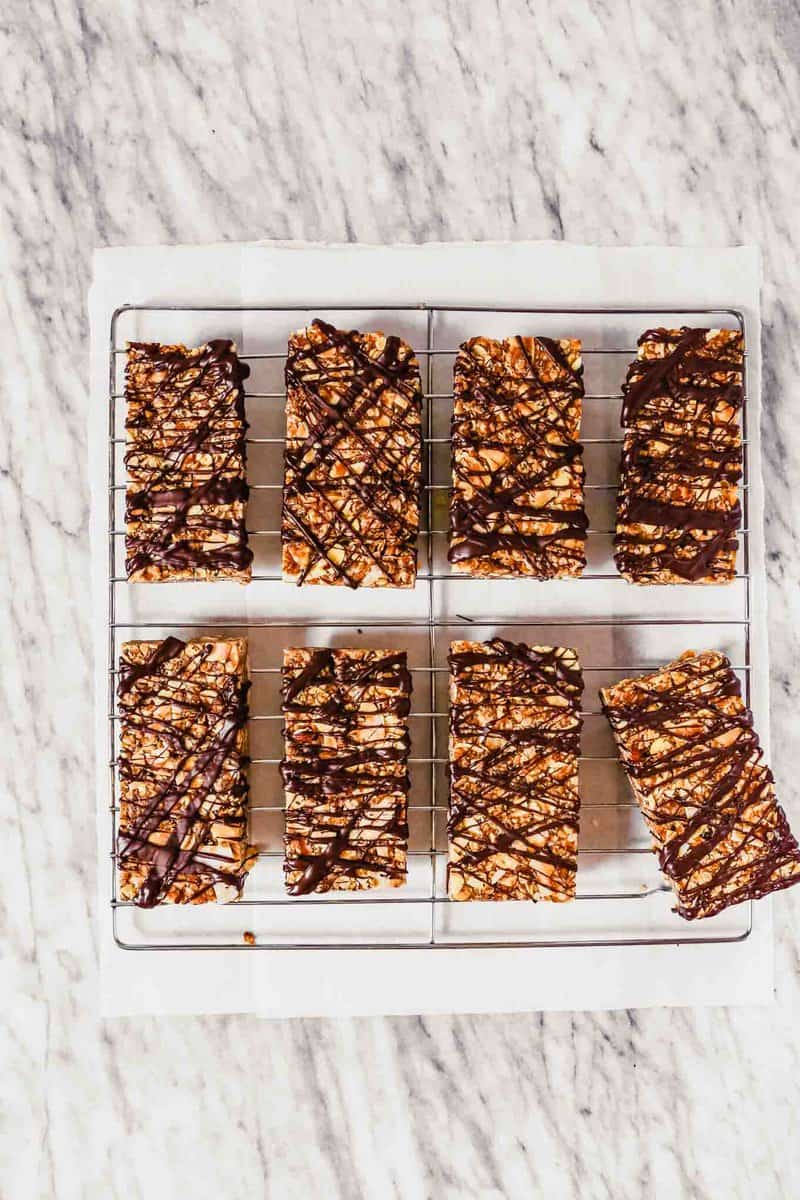 Photograph of homemade chewy granola bars stacked on top of each other on wax paper on a marble table.
