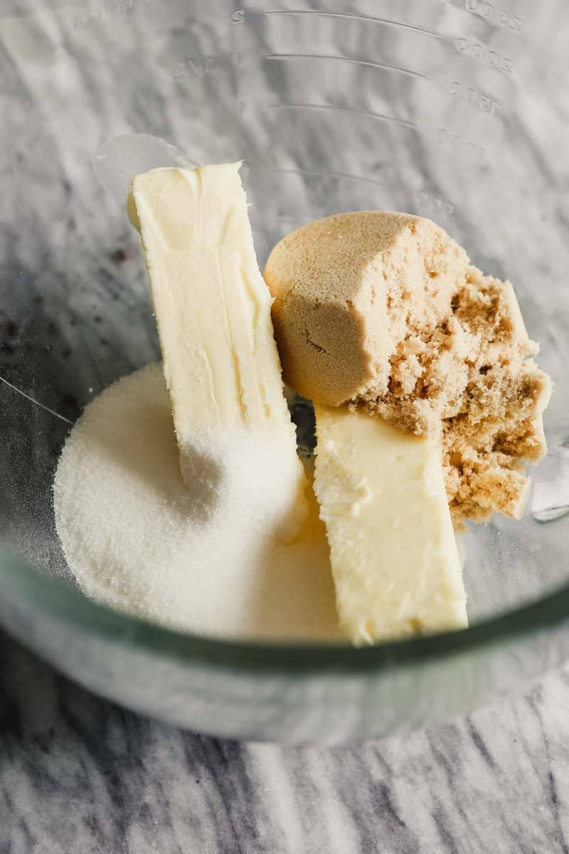 Photograph of butter, sugar and brown sugar in the bowl of a glass mixer