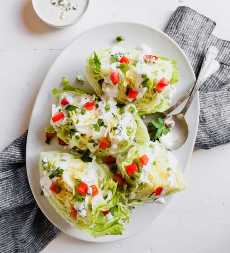 Photograph of a wedge salad with blue cheese dressing on a white plate set on a marble table