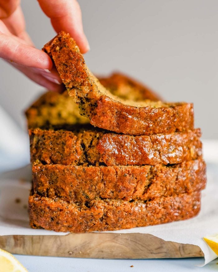 a hand picking up a piece of lemon poppyseed bread off of a stack of slices