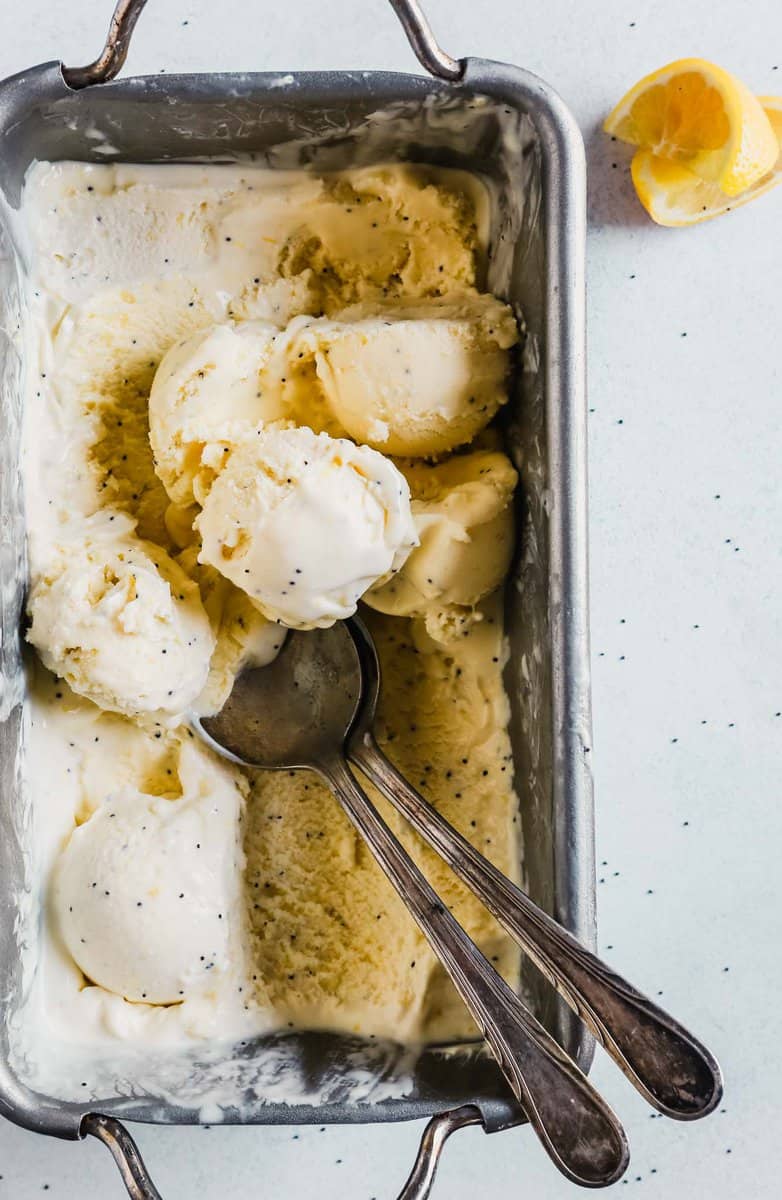 Photograph of a metal baking pan filled with lemon ice cream with scoops set on top and spoons in the ice cream