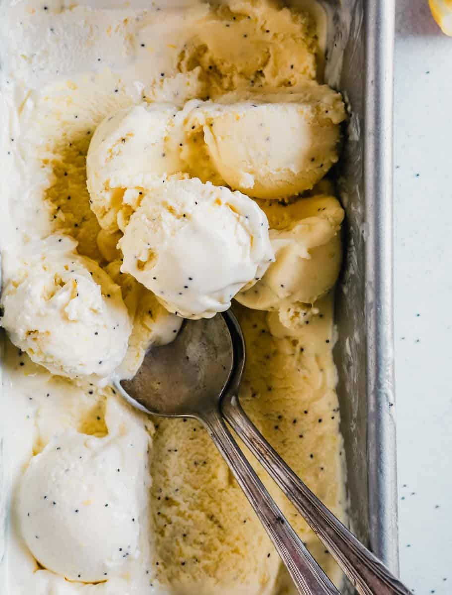 Photograph of a metal baking pan filled with lemon ice cream with scoops set on top and spoons in the ice cream