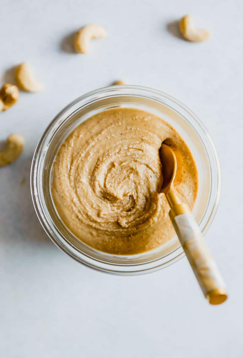 Photo of creamy cashew butter in a glass bowl with a gold spoon in it